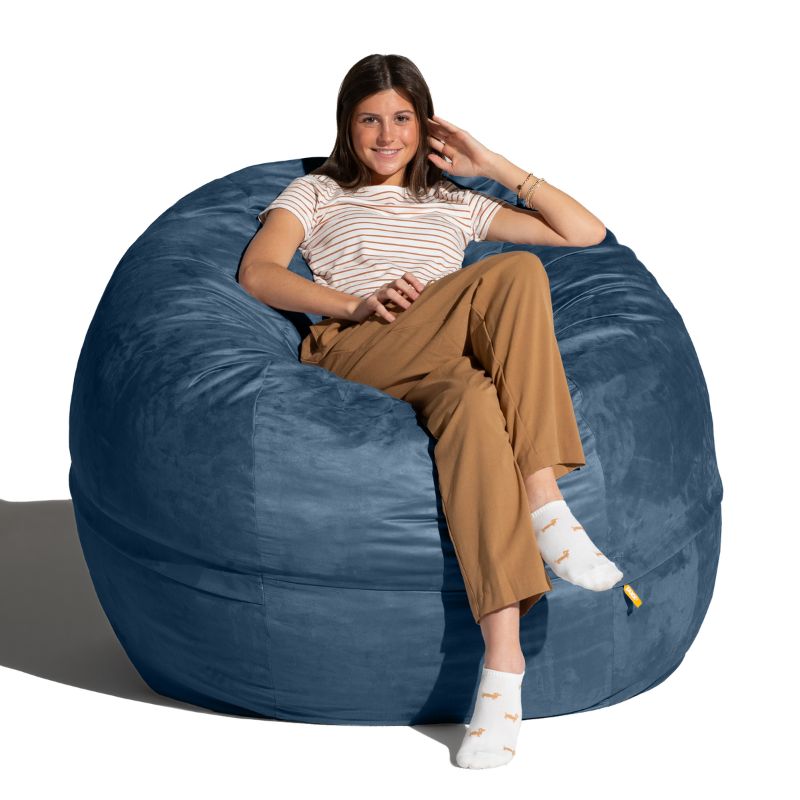 Young woman seated in a Navy microsuede Jaxx Saxx 5ft foam bean bag chair, a large bean bag chair with a removable washable cover