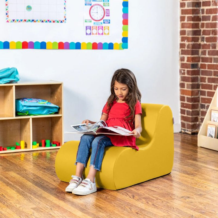 Young girl reading in a yellow Jaxx Midtown foam chair, a wipeable classroom soft seating chair for kids