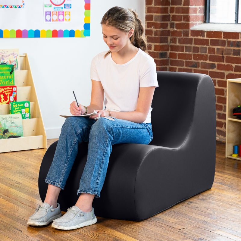 Student sitting in a black Jaxx Midtown foam chair while writing, a wipeable classroom soft seating chair for kids and adults