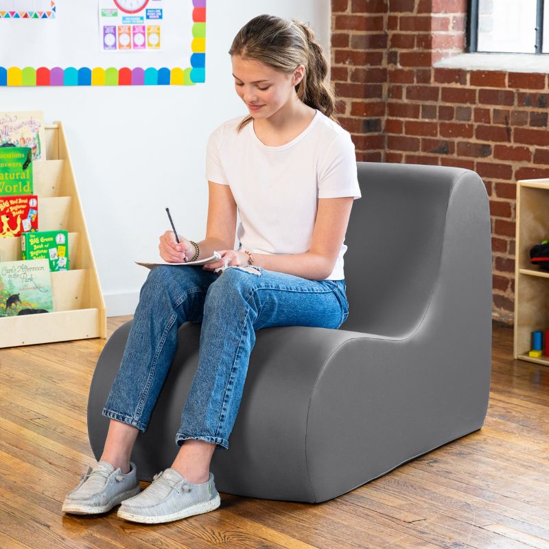 Student sitting in a charcoal Jaxx Midtown foam chair while writing, a wipeable classroom soft seating chair for kids and adults
