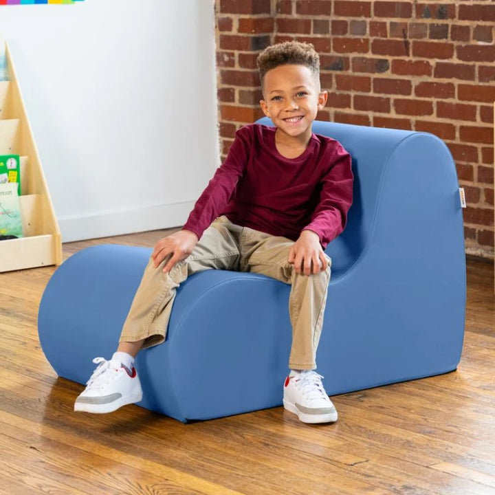 Young boy sitting in a blue Jaxx Midtown foam chair, a wipeable classroom soft seating chair for kids