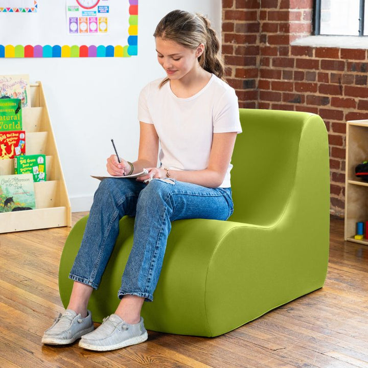 Student sitting in a green Jaxx Midtown foam chair while writing, a wipeable classroom soft seating chair for kids and adults