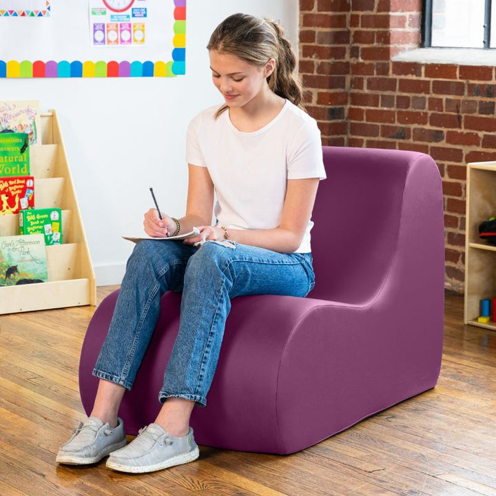 Student sitting in a purple Jaxx Midtown foam chair while writing, a wipeable classroom soft seating chair for kids and adults