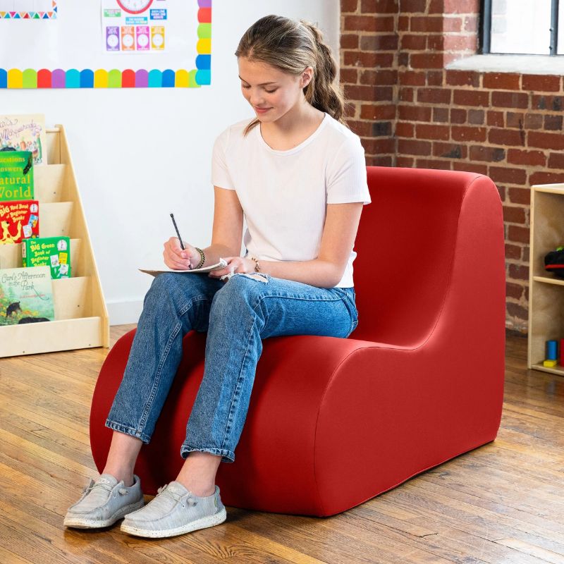 Student sitting in a red Jaxx Midtown foam chair while writing, a wipeable classroom soft seating chair for kids and adults
