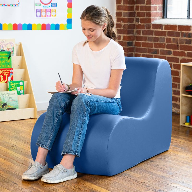 Student sitting in a royal blue Jaxx Midtown foam chair while writing, a wipeable classroom soft seating chair for kids and adults