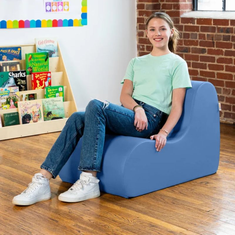 Teen sitting in a blue Jaxx Midtown foam chair, a wipeable classroom soft seating chair for kids and adults