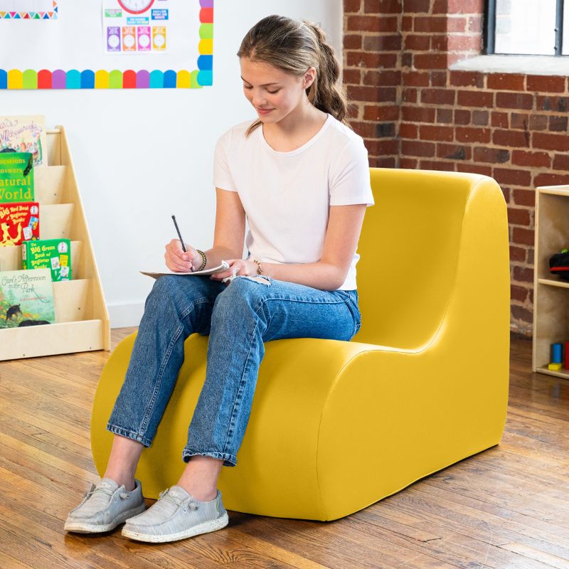 Student sitting in a yellow Jaxx Midtown foam chair while writing, a wipeable classroom soft seating chair for kids and adults