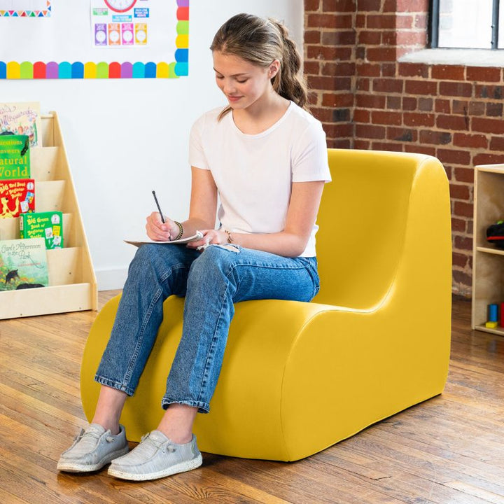 Student sitting in a yellow Jaxx Midtown foam chair while writing, a wipeable classroom soft seating chair for kids and adults