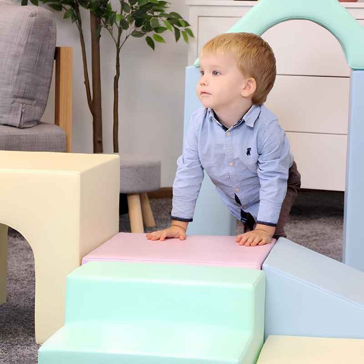 A toddler boy playing on the IGLU Foam Play Set Creativity in Light Pastel, building gross motor skills through climbing