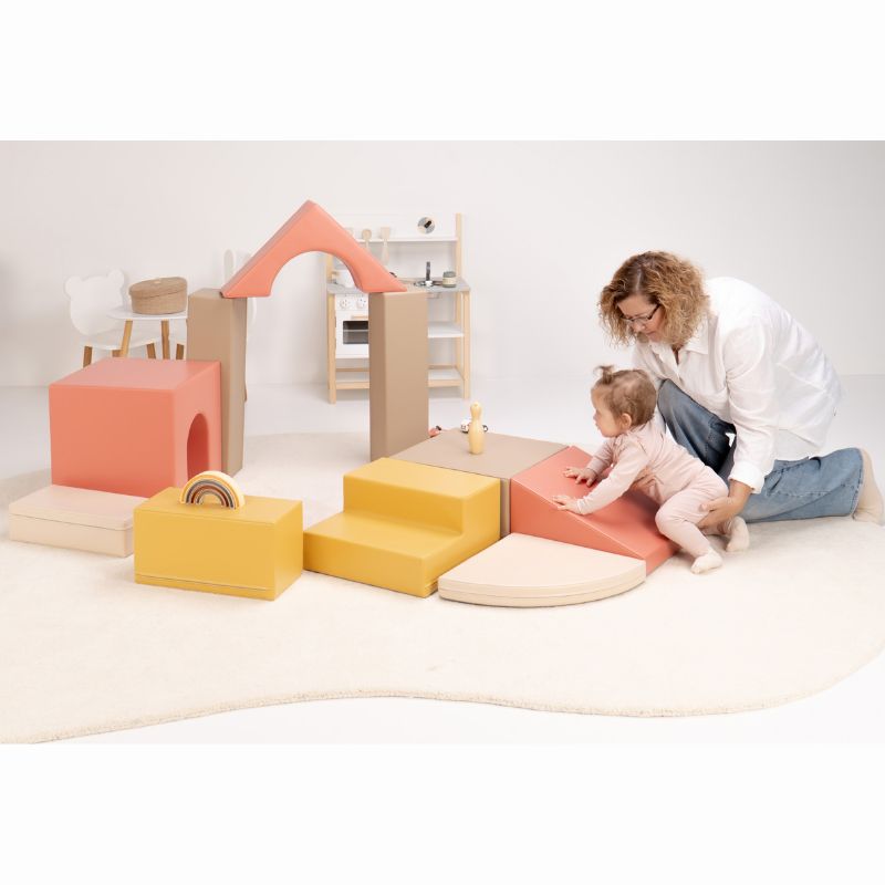 Baby climbing the ramp of the IGLU Foam Play Set - Creativity with a caregiver's support, the full soft play set arranged behind