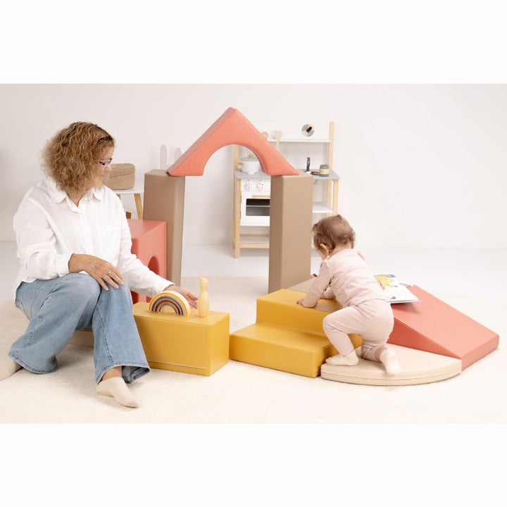 Baby climbing the steps toward the ramp of the IGLU Foam Play Set - Creativity, with the arch assembled behind as a soft play set