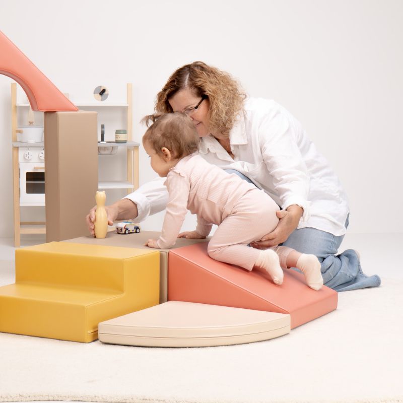 Baby crawling up the soft ramp of the IGLU Foam Play Set - Creativity while a caregiver offers gentle support