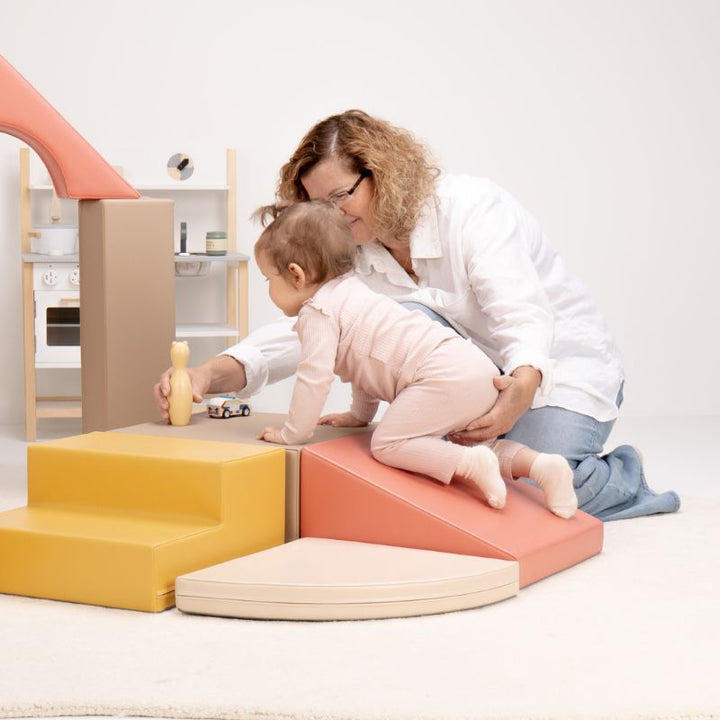Baby crawling up the soft ramp of the IGLU Foam Play Set - Creativity while a caregiver offers gentle support