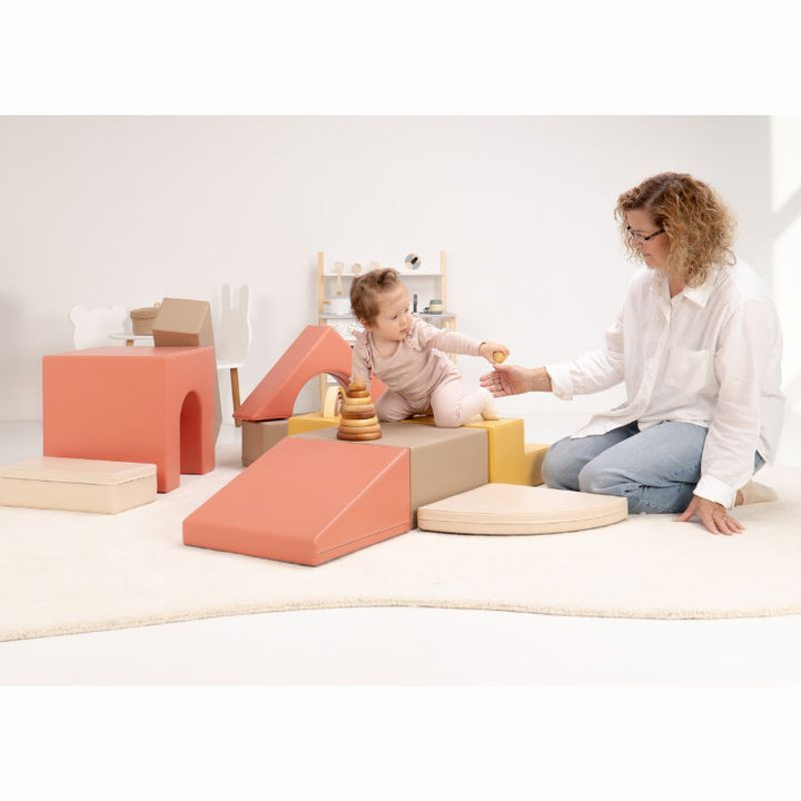 Baby sitting on the IGLU Foam Play Set - Creativity and handing a ball to a caregiver, encouraging social play on a soft play set