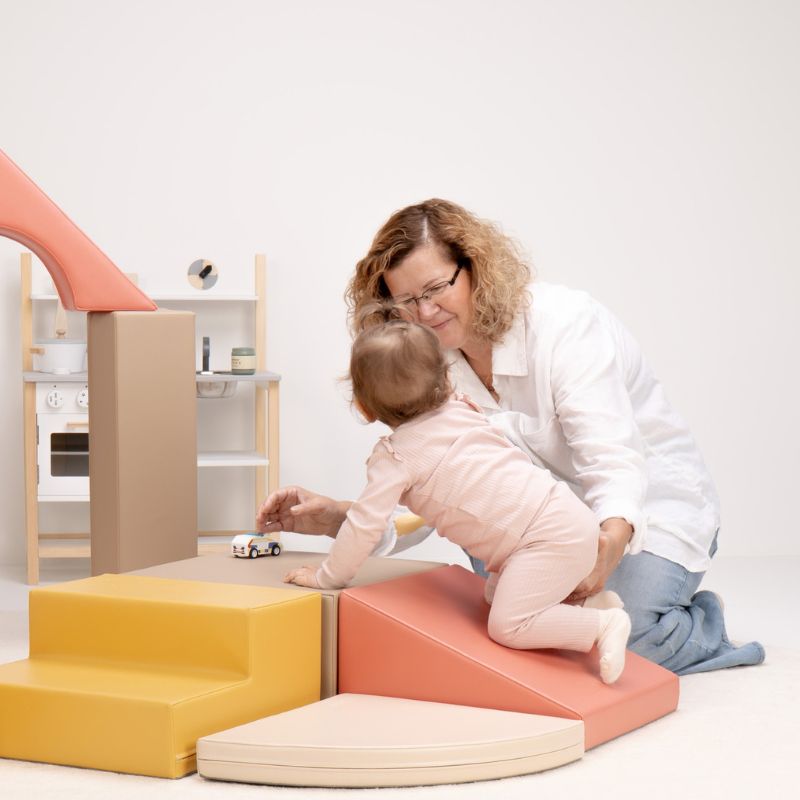 Close-up of a baby climbing the IGLU Foam Play Set - Creativity ramp toward a toy car, building gross motor skills on foam climbing blocks