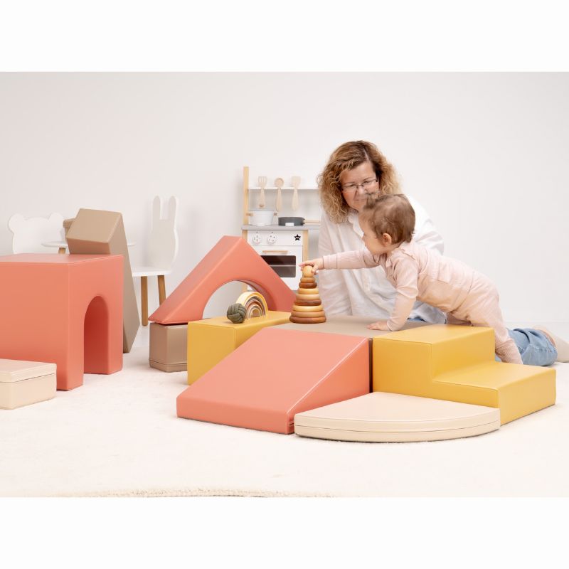 Baby leaning over the IGLU Foam Play Set - Creativity platform to reach a wooden ring stacker during hands-on baby soft play