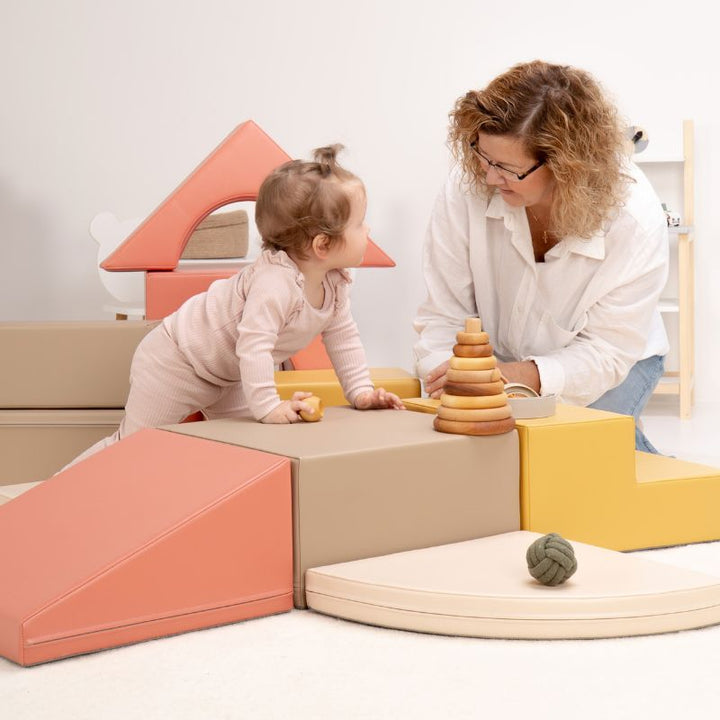 Baby standing at the IGLU Foam Play Set - Creativity platform beside a ring stacker, sharing playtime with a caregiver