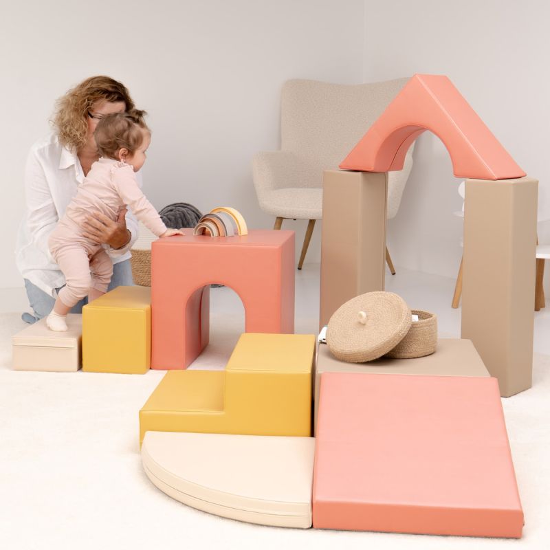 Caregiver supporting a baby stepping up the IGLU Foam Play Set - Creativity steps toward the tunnel cube, building gross motor skills