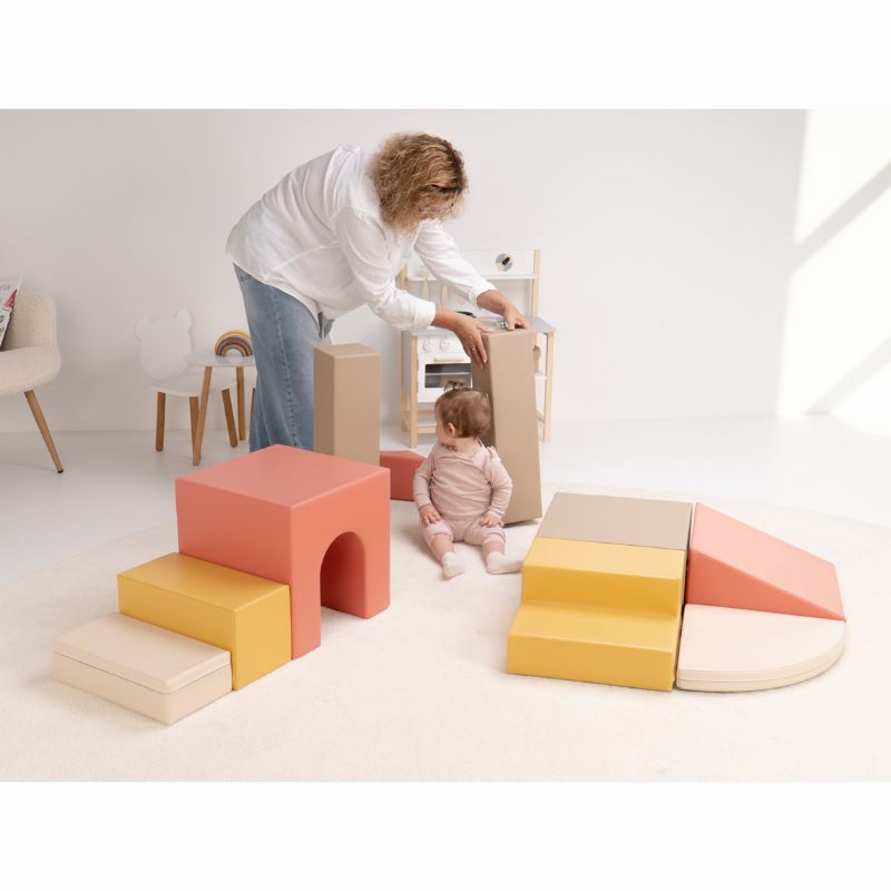 Caregiver setting up a tall pillar from the IGLU Foam Play Set - Creativity as a baby sits among the modular soft play blocks