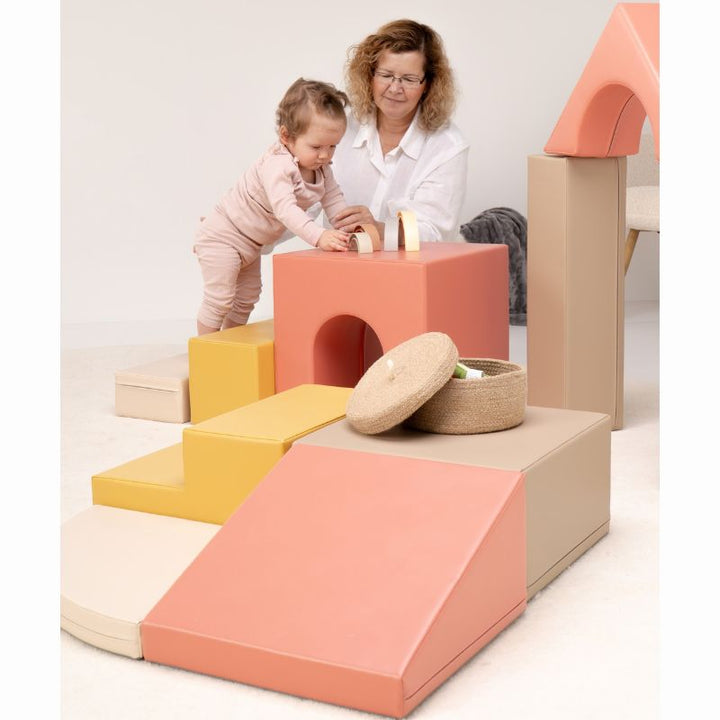 Toddler standing at the tunnel cube of the IGLU Foam Play Set - Creativity, stacking rainbow pieces during imaginative soft play