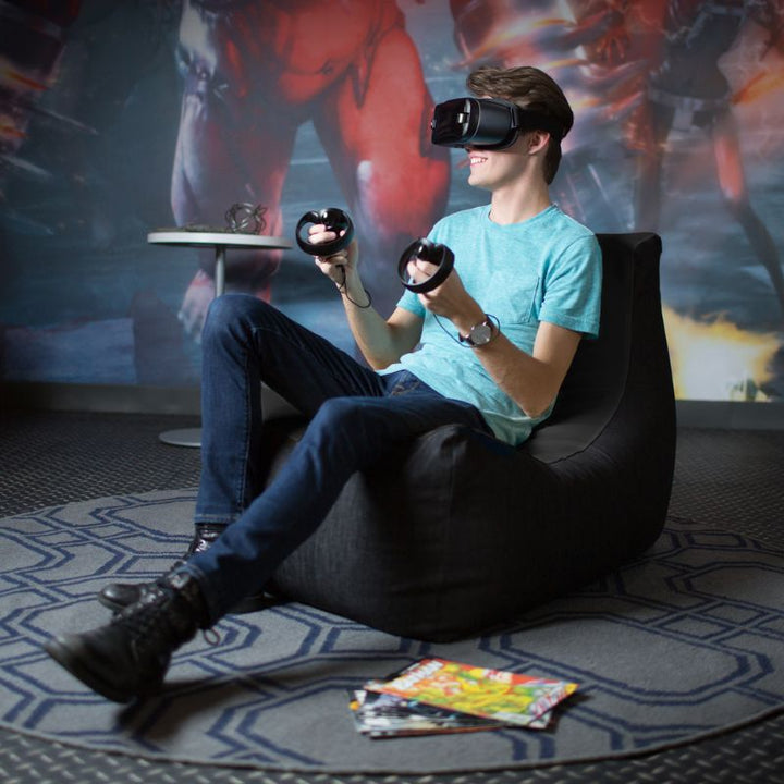A teen uses a VR headset while seated in the Jaxx Pixel gaming bean bag chair in black, a durable seat for game rooms