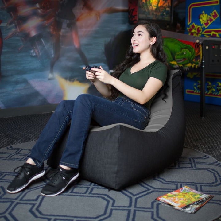 A teen relaxes in the Jaxx Pixel gaming bean bag chair in charcoal while playing video games, sensory seating for kids