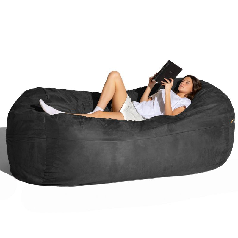 Woman reading on the Jaxx 7 ft giant bean bag chair in black microsuede, a cozy lounger for calm corners and living rooms