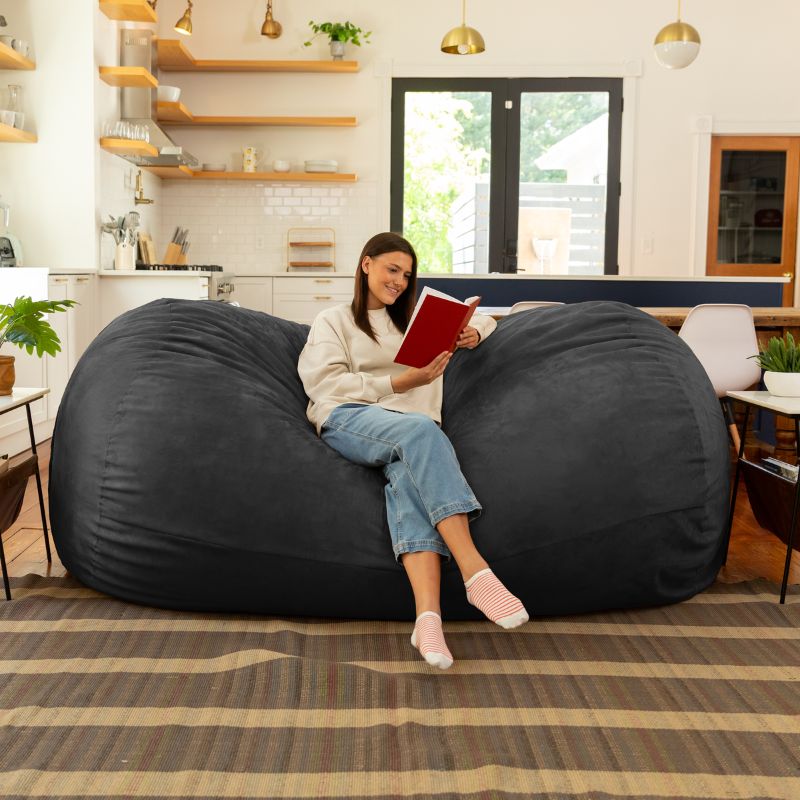 Woman reading on the Jaxx 7 ft giant bean bag chair in black microsuede in a styled living space