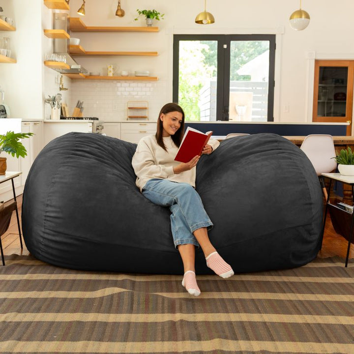 Woman reading on the Jaxx 7 ft giant bean bag chair in black microsuede in a styled living space