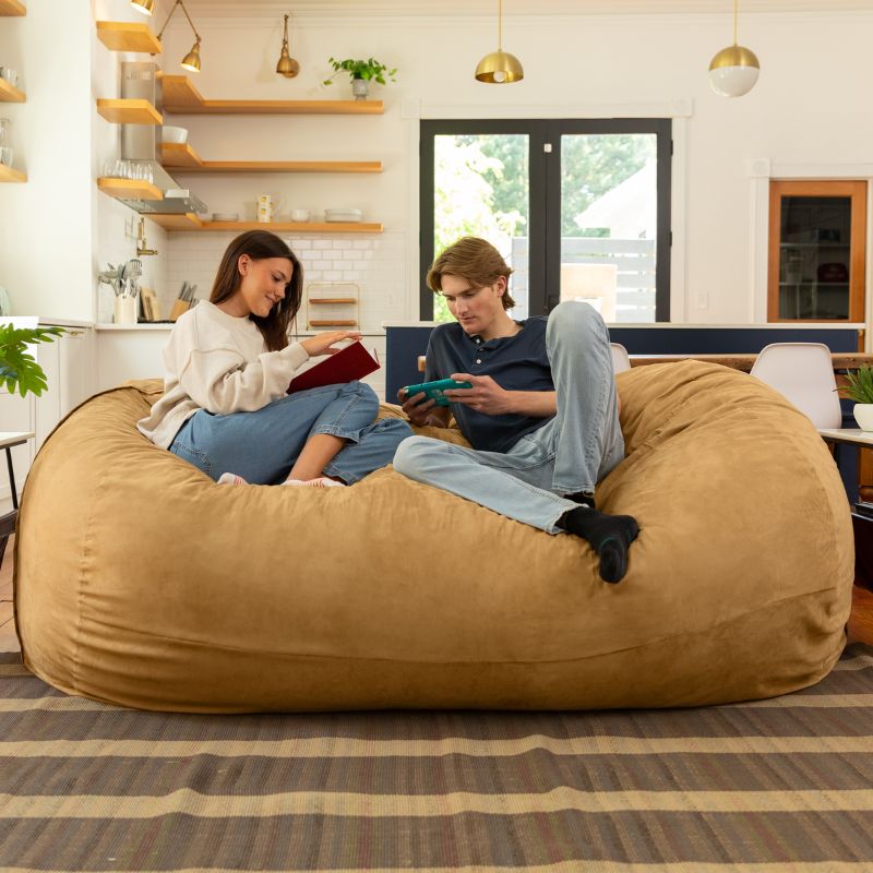 Couple reading and gaming together on the Jaxx giant bean bag chair in camel microsuede in a styled living space