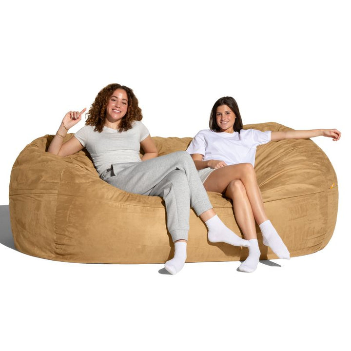 Two people lounging on the Jaxx giant bean bag chair in camel microsuede, a cozy 7 ft seat for family rooms