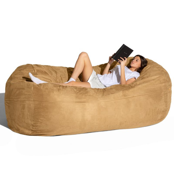 Woman reading on the Jaxx giant bean bag chair in camel microsuede, an oversized seat for family rooms