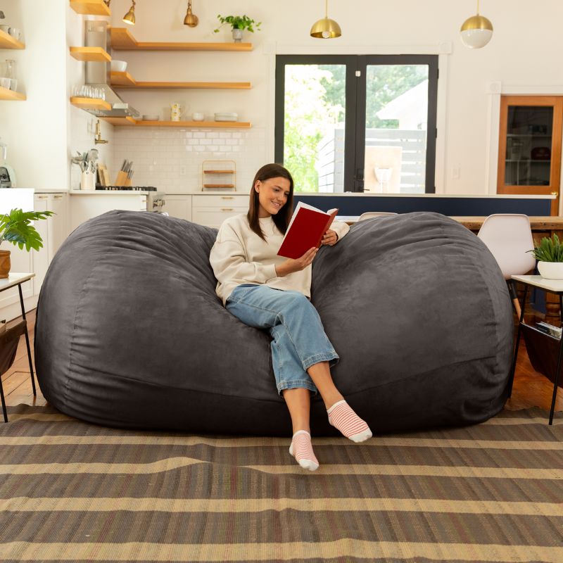 Woman reading on the Jaxx 7 ft giant bean bag chair in charcoal microsuede in a styled living space