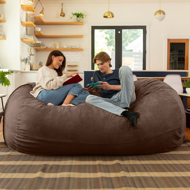 Couple reading and gaming together on the Jaxx giant bean bag chair in chocolate microsuede in a styled living space