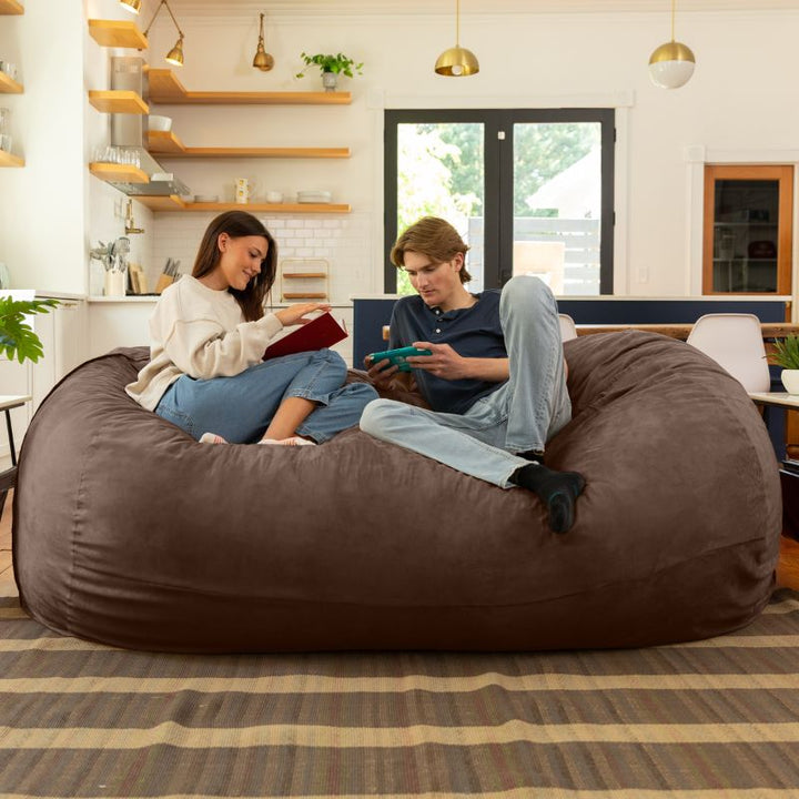 Couple reading and gaming together on the Jaxx giant bean bag chair in chocolate microsuede in a styled living space