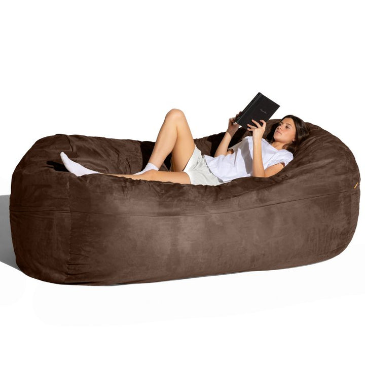 Woman reading on the Jaxx giant bean bag chair in chocolate microsuede for calm corners and family rooms