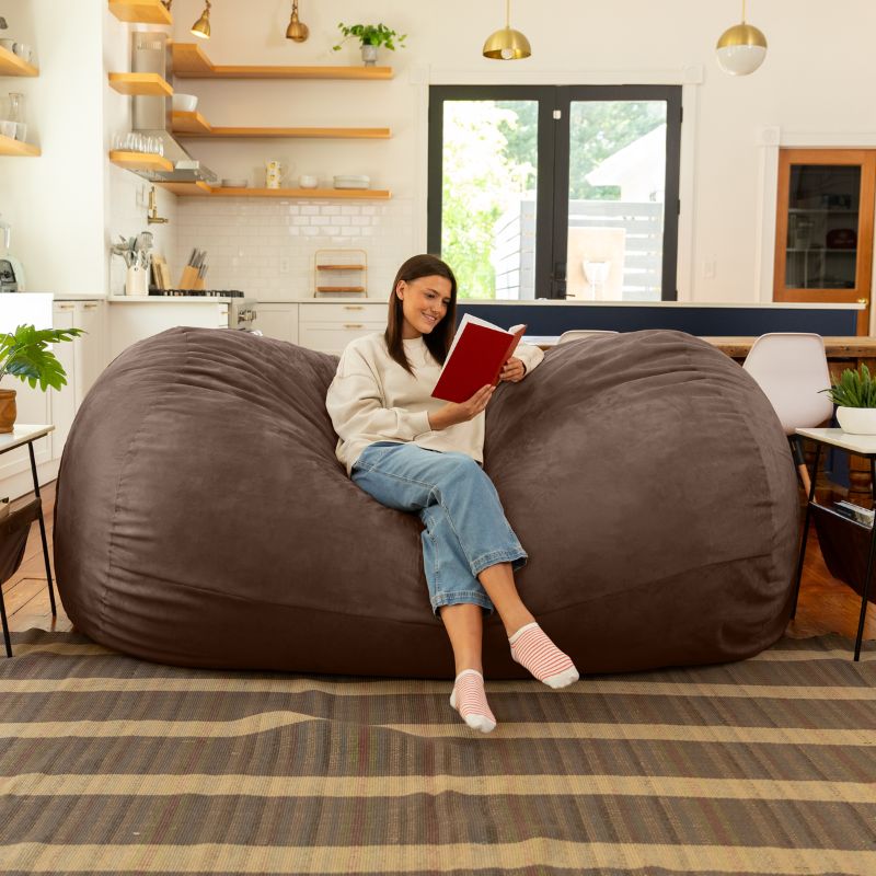 Woman reading on the Jaxx giant bean bag chair in chocolate microsuede in a styled living space