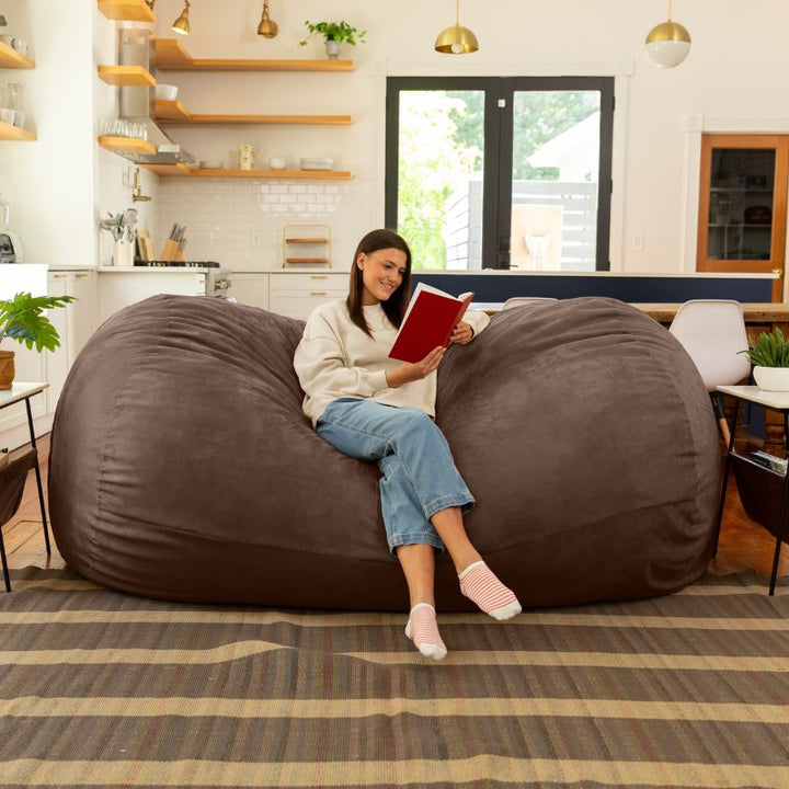 Woman reading on the Jaxx giant bean bag chair in chocolate microsuede in a styled living space