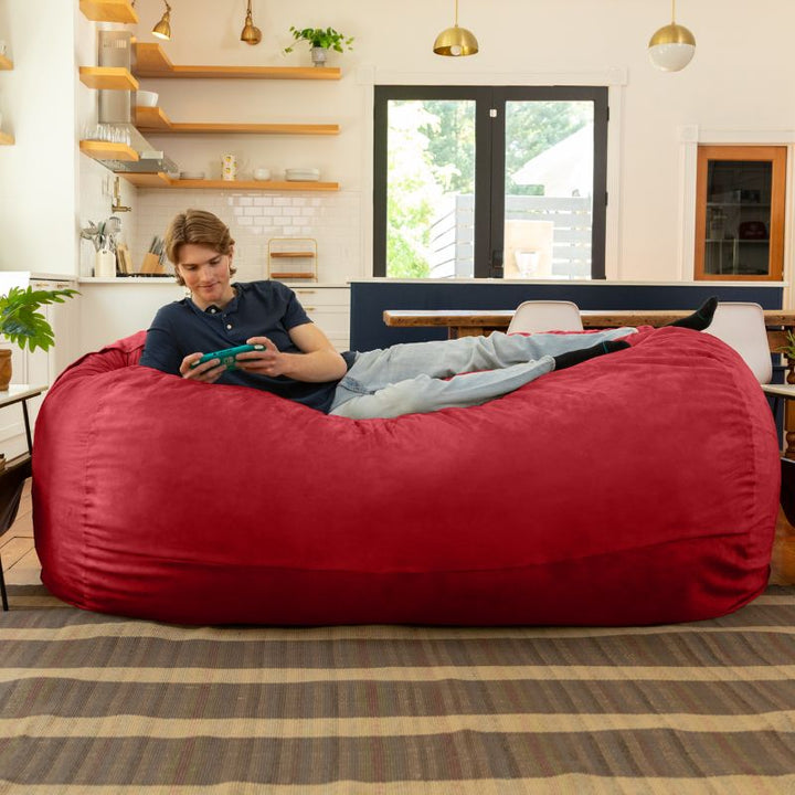 Man playing a handheld game on the Jaxx 7 ft giant bean bag chair in cinnabar microsuede in a styled living space