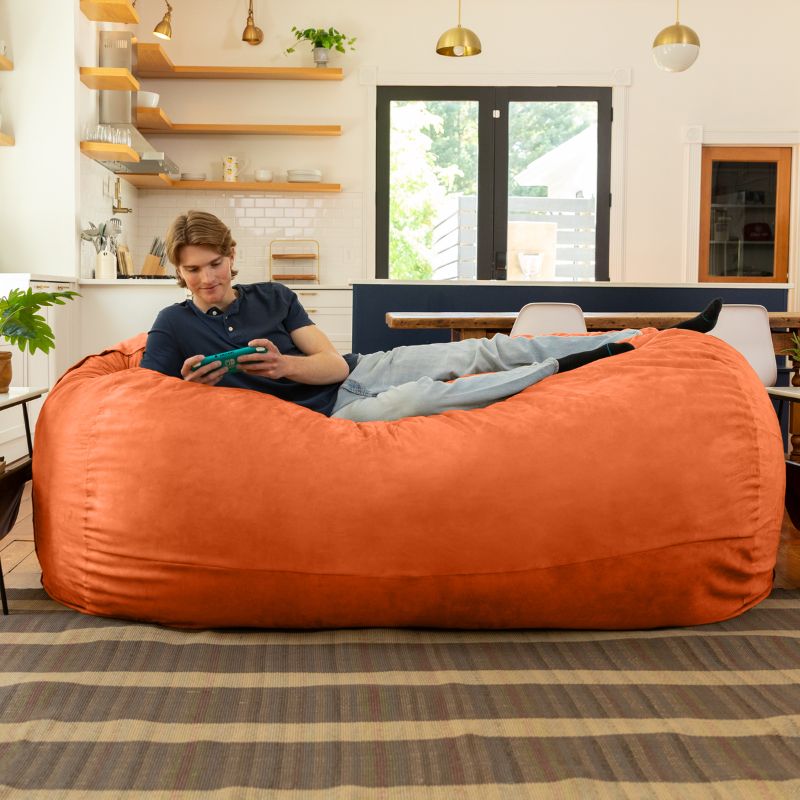 Man playing a handheld game on the Jaxx giant bean bag chair in mandarin microsuede in a styled living space