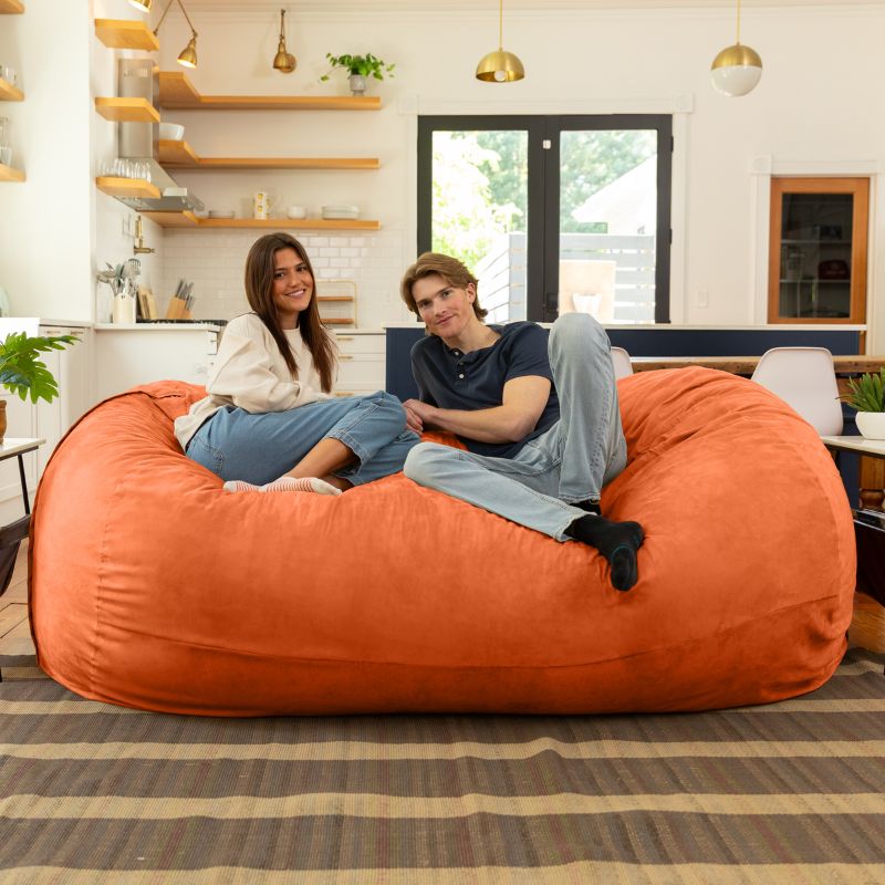 Couple relaxing together on the Jaxx giant bean bag chair in mandarin microsuede in a styled living space