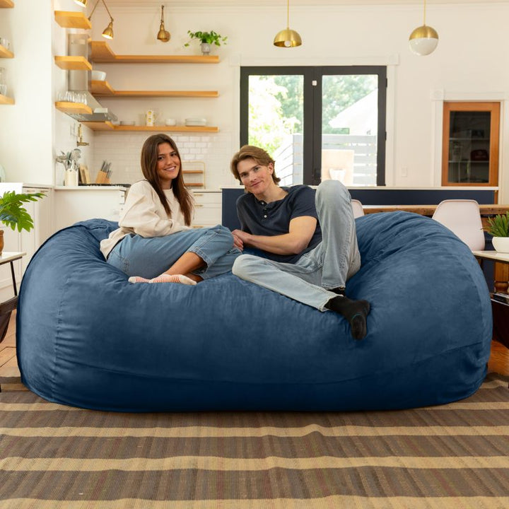 Couple relaxing together on the Jaxx 7 ft giant bean bag chair in navy microsuede in a styled living space