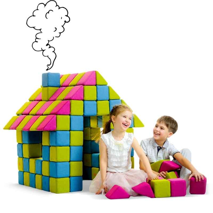 Two children playing beside a house built from JollyHeap Joy giant magnetic building blocks in pink, lime and blue, showing group play with the set