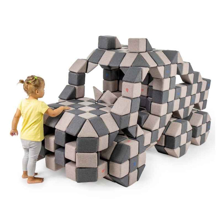 Child standing beside a large truck structure built from JollyHeap giant magnetic building blocks in grey and tan