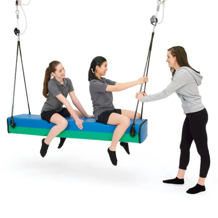 Two riders share the Southpaw Glider Bolster Swing in the standard size while a therapist guides its smooth vestibular gliding motion