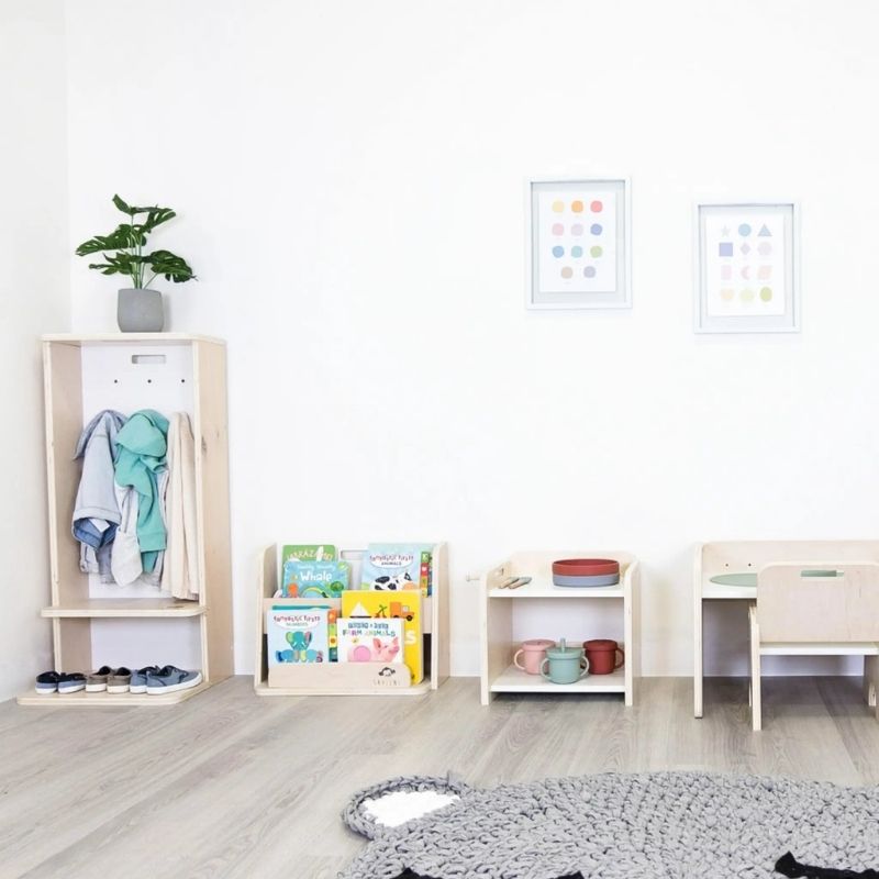 Sapiens Child Guava Montessori Bookshelf in an indoor Montessori room set, showing how the forward-facing bookshelf pairs with other Sapiens Child furniture pieces for a complete child-sized environment