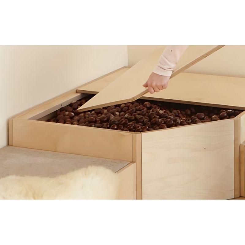 Adult hand lifting one section of the HABA Pro Grow.upp sensory bath platform lid to reveal a chestnut-filled tactile sensory bath in a corner installation