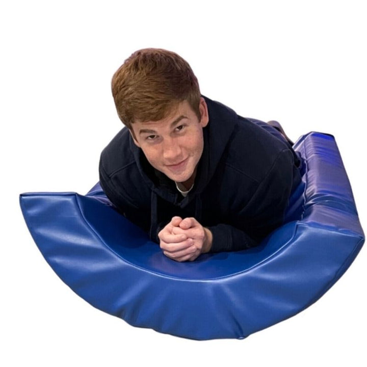TFH Half Barrel Rocker in blue vinyl, a vestibular sensory rocker shown supporting a user lying face down for rocking and balance play