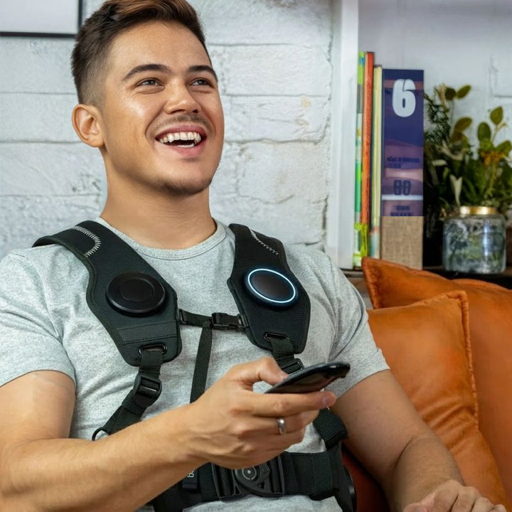Man relaxing on a couch at home with his phone while wearing the Woojer Vest 4 haptic vest as a wearable vibroacoustic experience