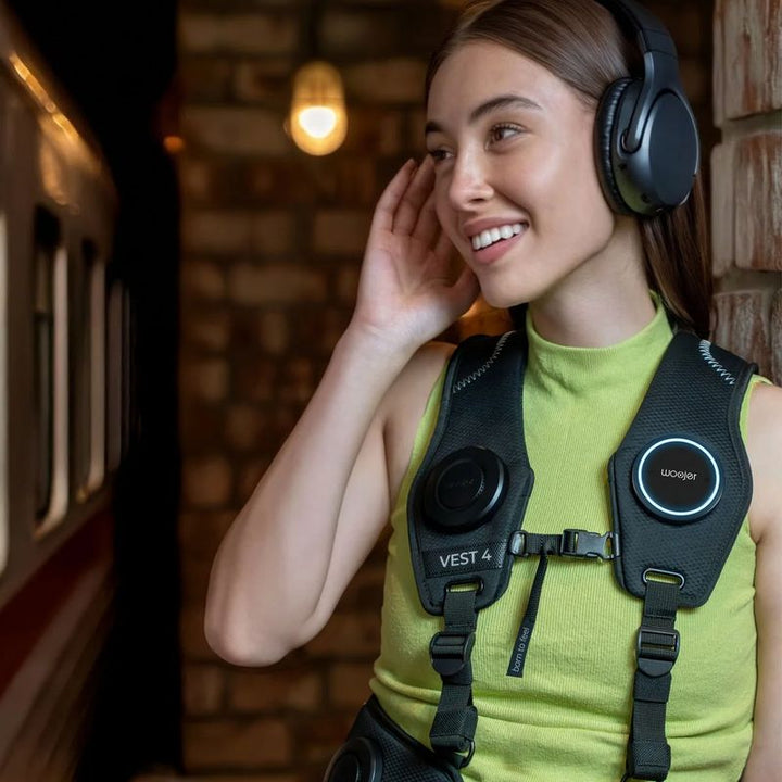 Woman listening to music on headphones while wearing the Woojer Vest 4 haptic vest, feeling every beat as sensory input